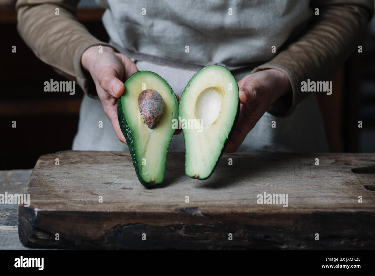 Woman holding halved avocado, mid section Stock Photo