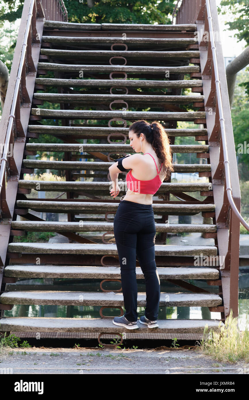 Young female runner standing on stairway looking at smartphone armband Stock Photo