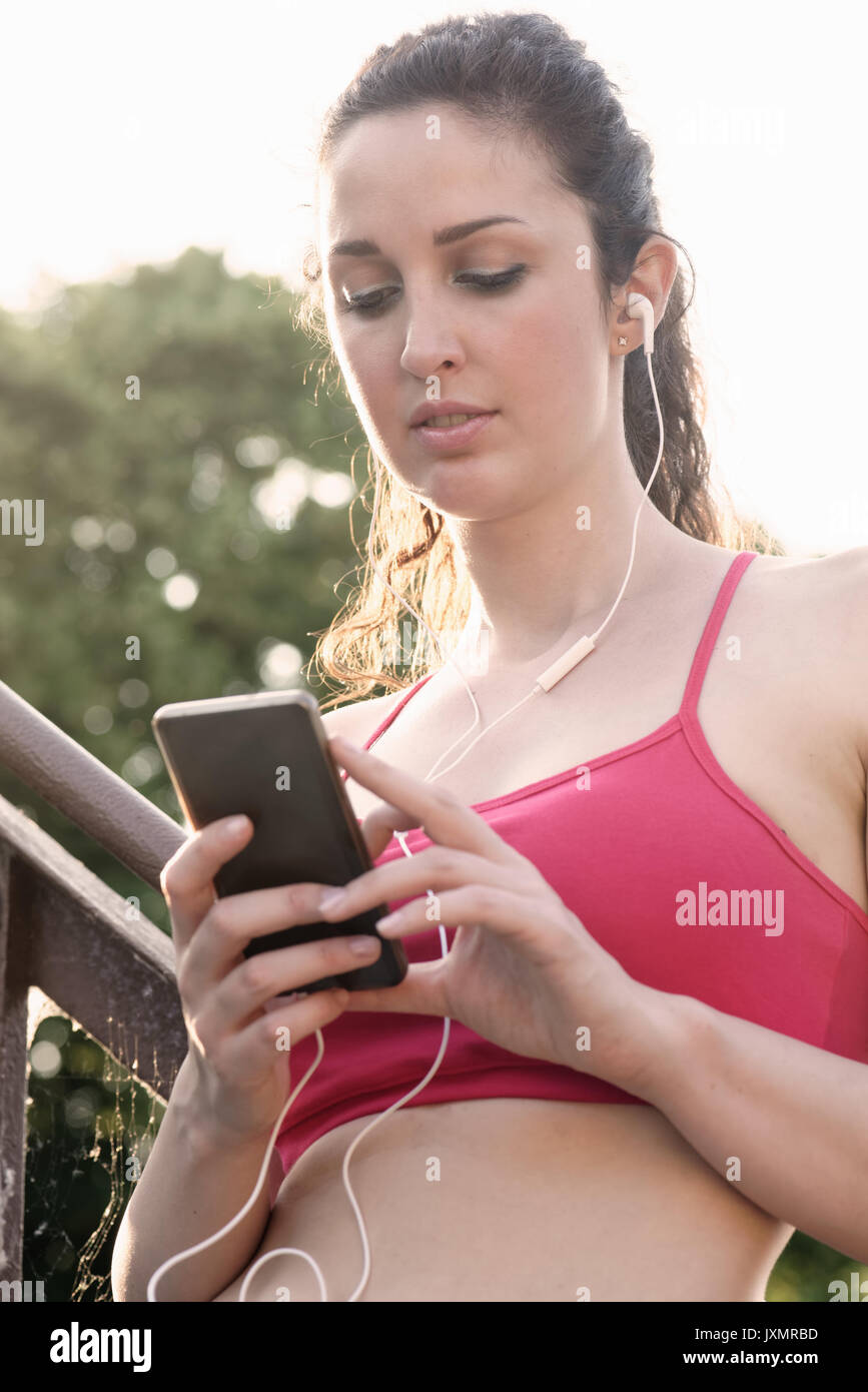 Young female runner on stairway wearing earphones and looking at smartphone Stock Photo