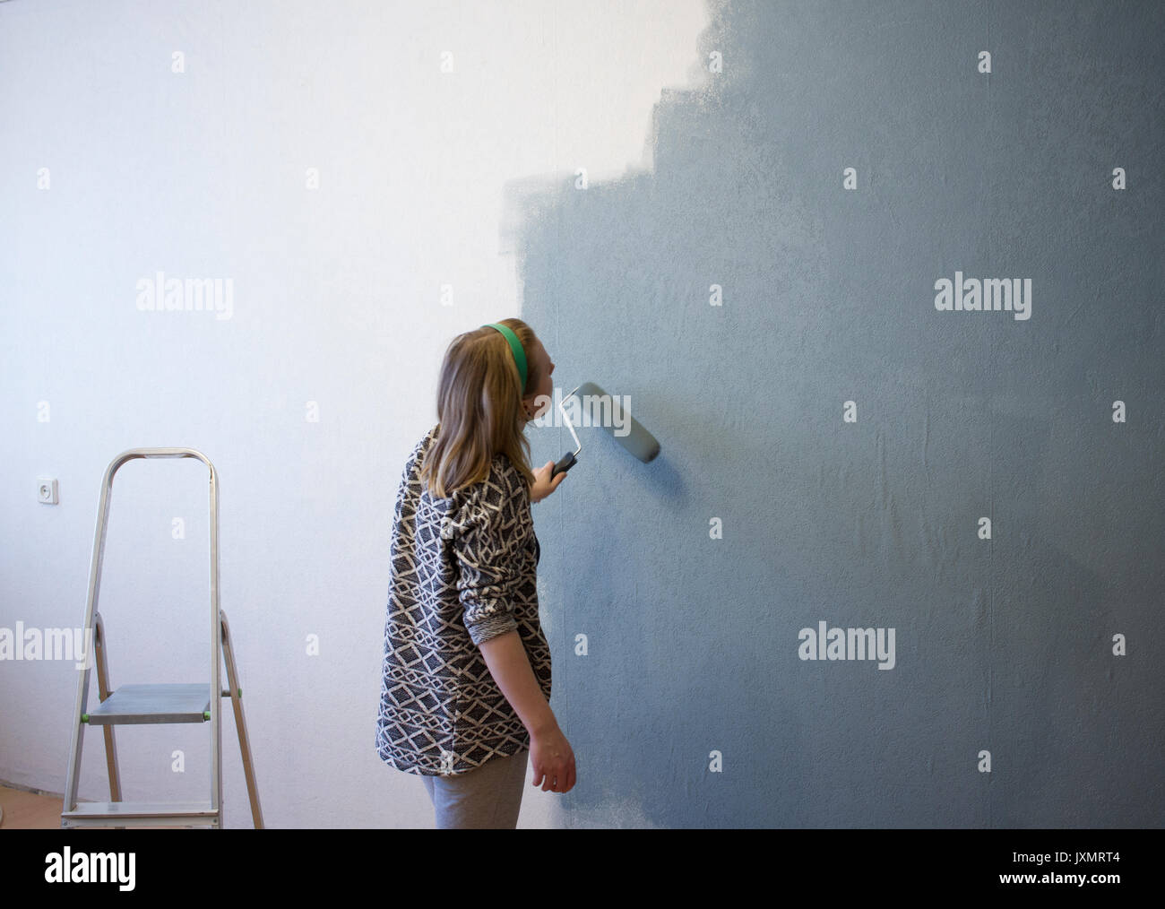 Young woman applying grey paint to interior wall at home Stock Photo