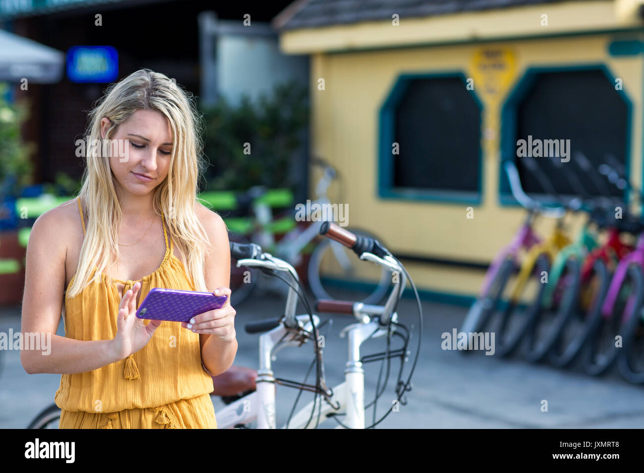 Young woman with long blond hair looking at smartphone by bicycle, Santa Monica, California, USA Stock Photo