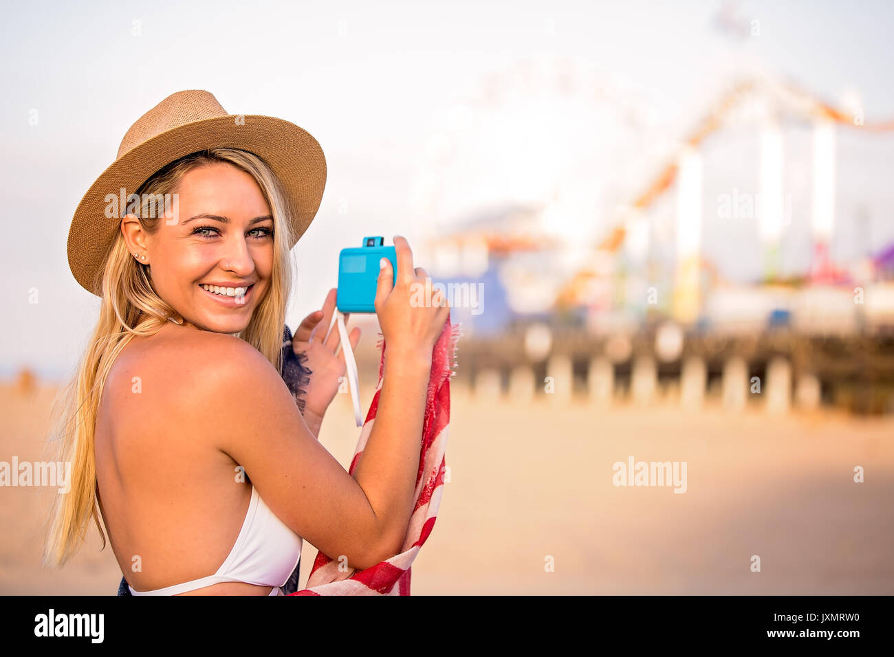 Portrait of young woman in bikini top photographing beach amusement park, Santa Monica, California, USA Stock Photo