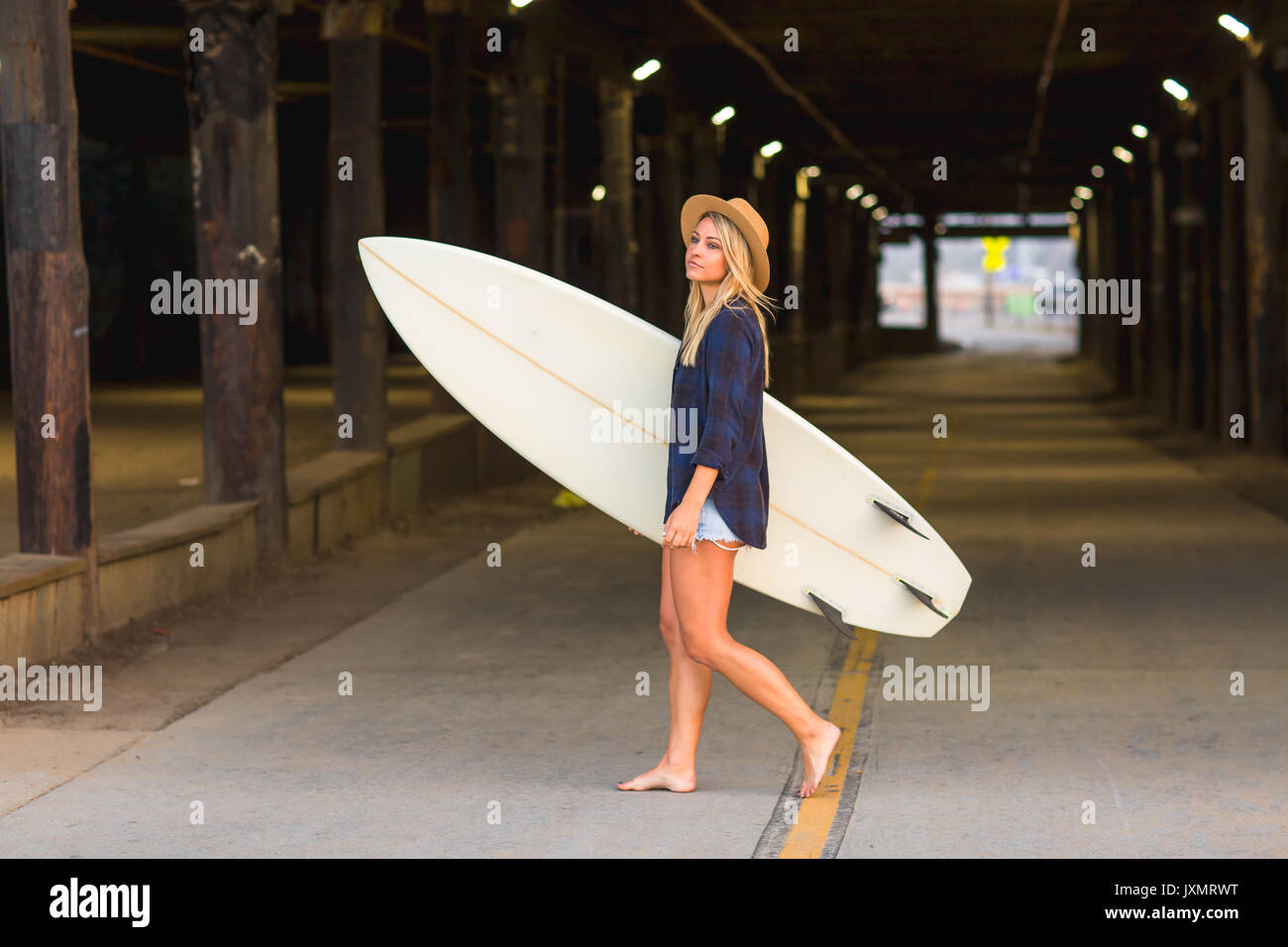 Young female surfer carrying surfboard in underpass, Santa Monica, California, USA Stock Photo