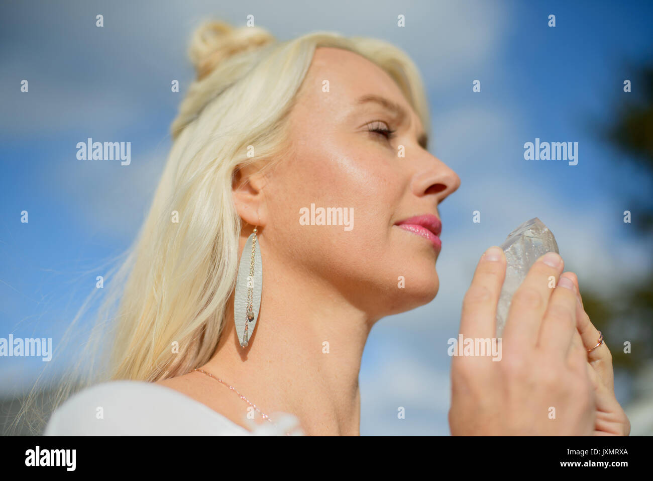 Mid adult woman meditating holding crystal against blue sky Stock Photo