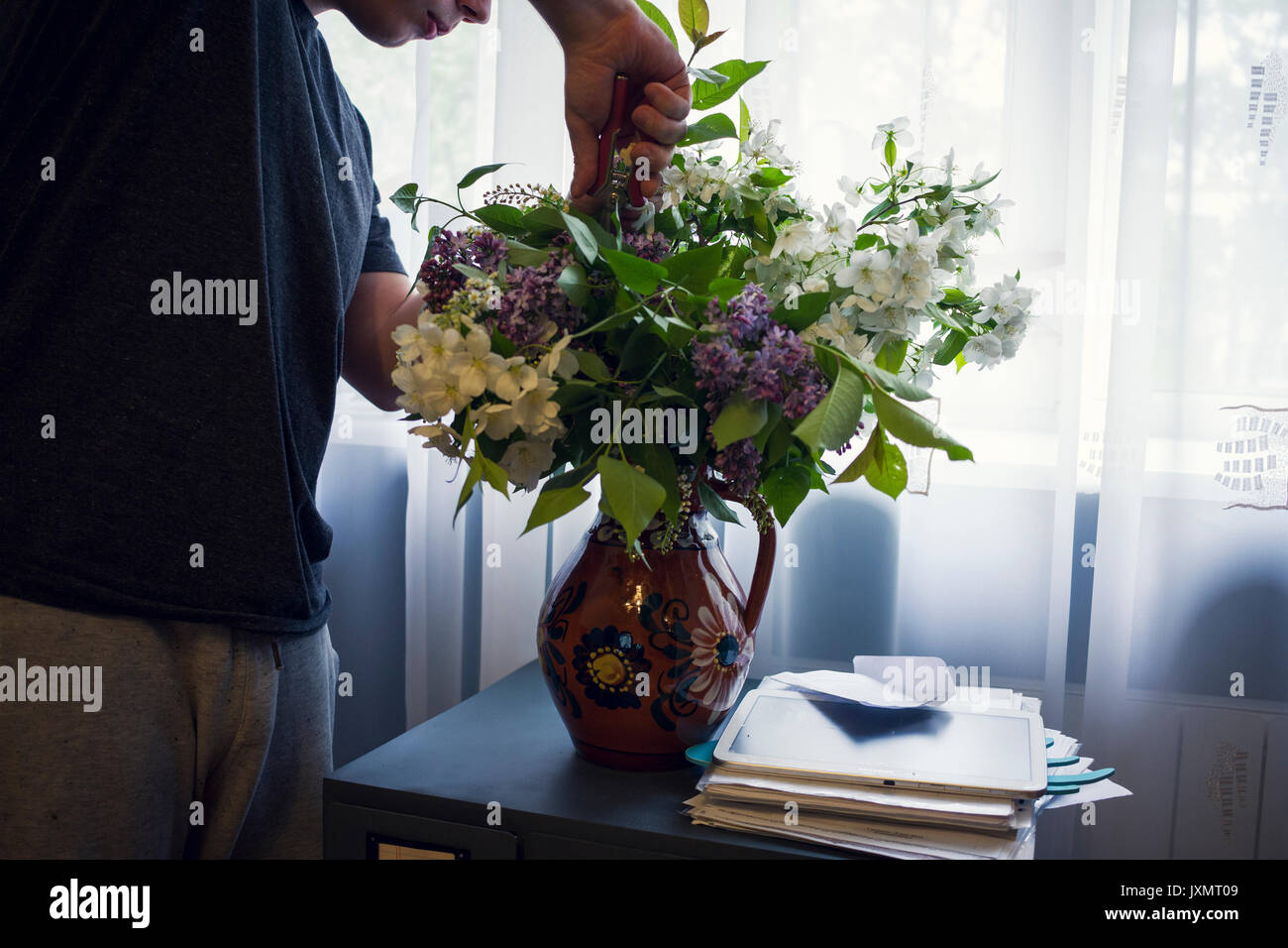Mid section of young man arranging vase of flowers in front of window Stock Photo
