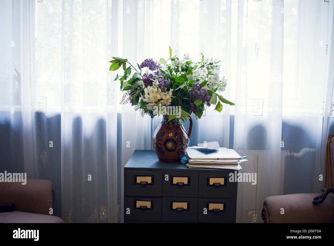 Vase of flowers on drawers in front of window Stock Photo