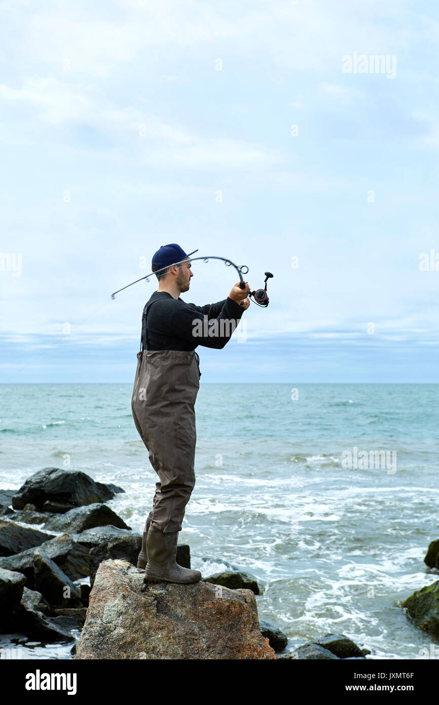 Young man on rock casting fishing rod to sea Stock Photo