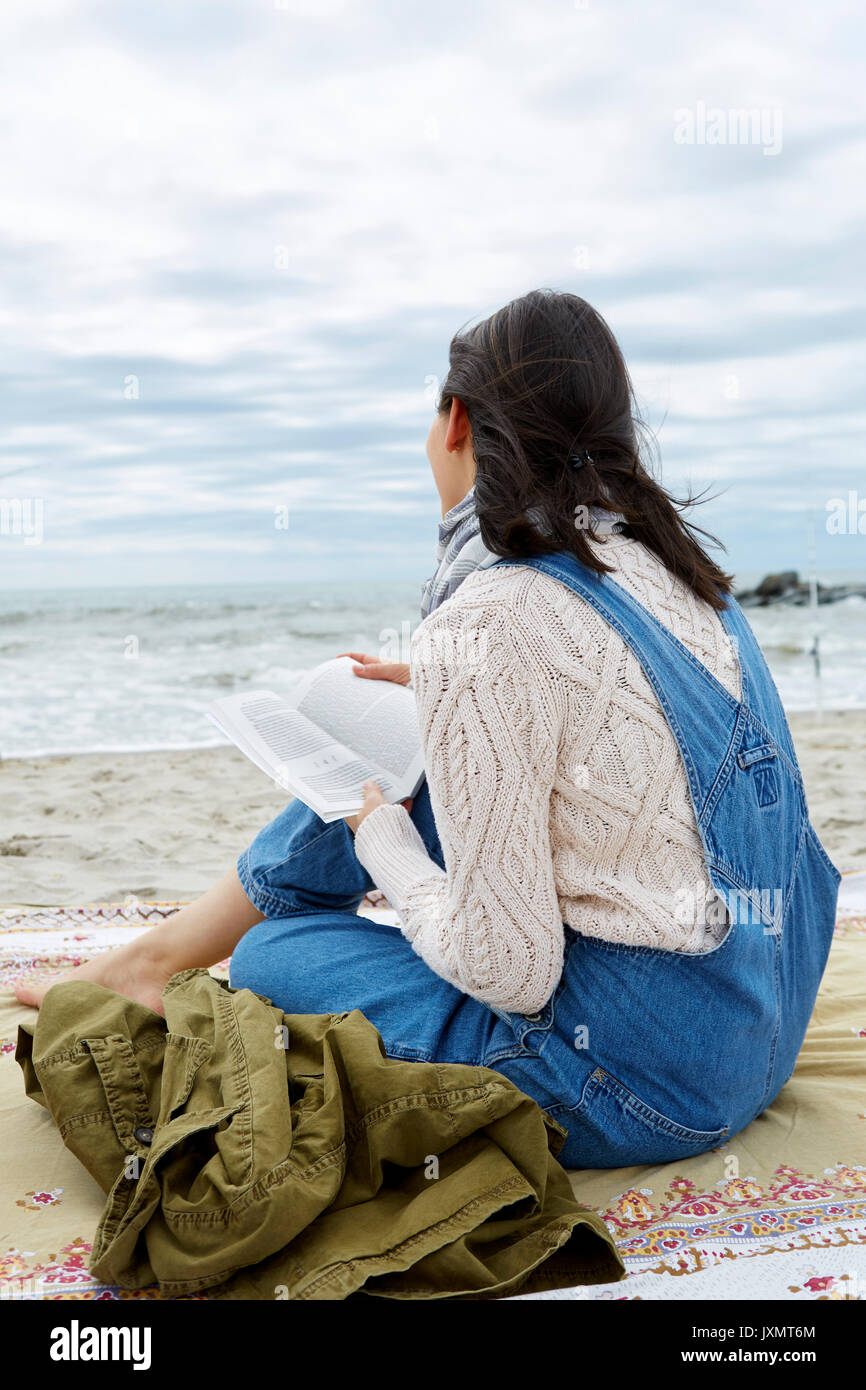 Young woman sitting on beach looking out at sea Stock Photo - Alamy