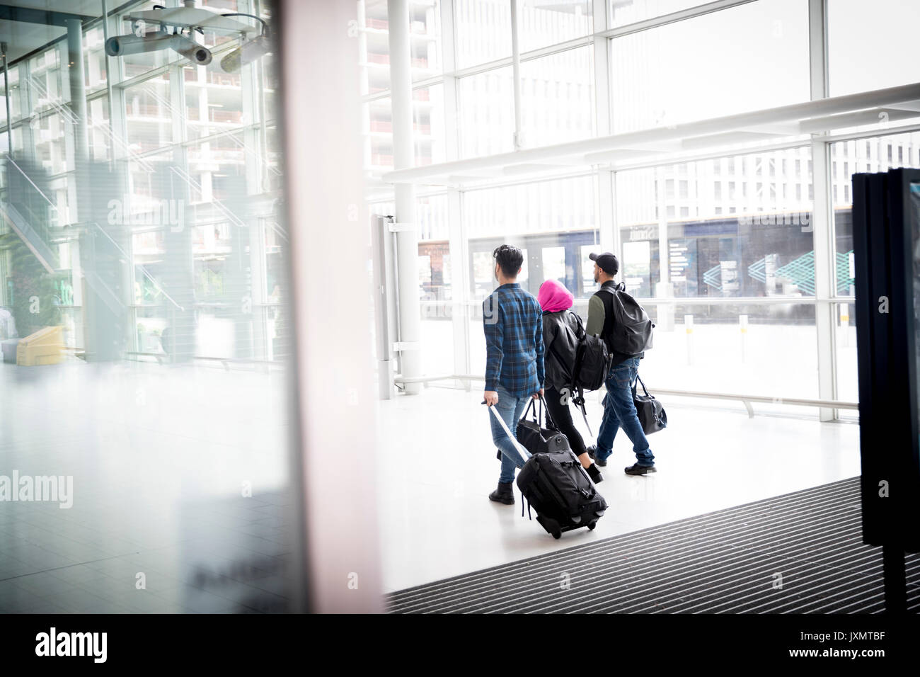 Three friends, walking outdoors, pulling wheeled suitcase, rear view Stock Photo