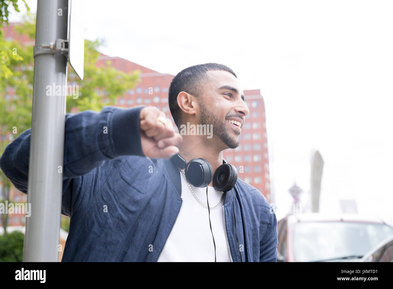 Young man leaning against lamppost, headphones around neck, smiling Stock Photo