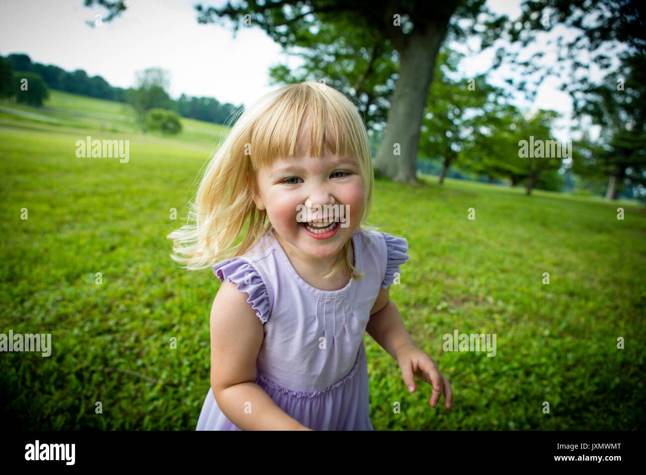 Portrait of blond haired girl running in rural field Stock Photo