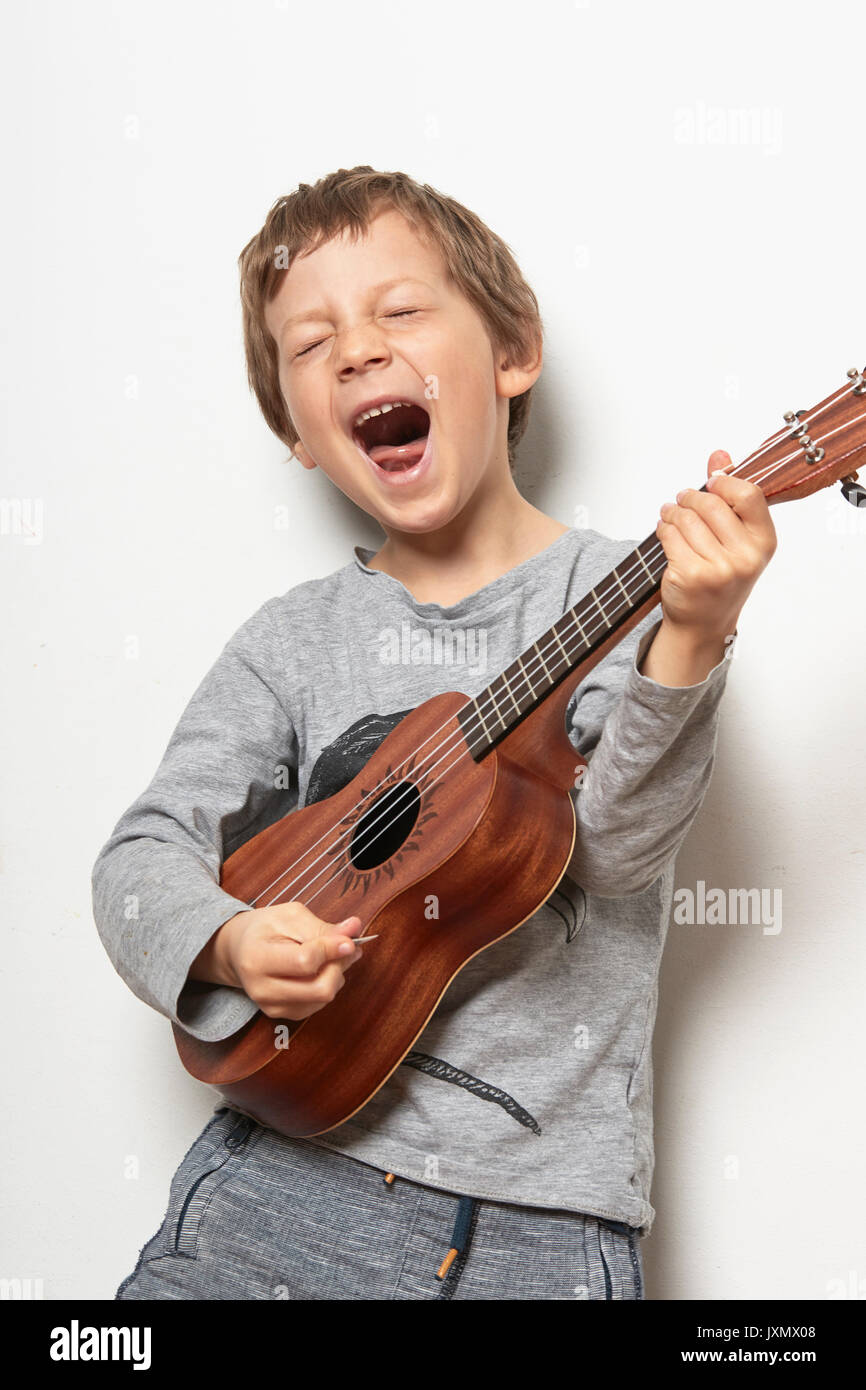 Boy playing ukulele, pulling face Stock Photo