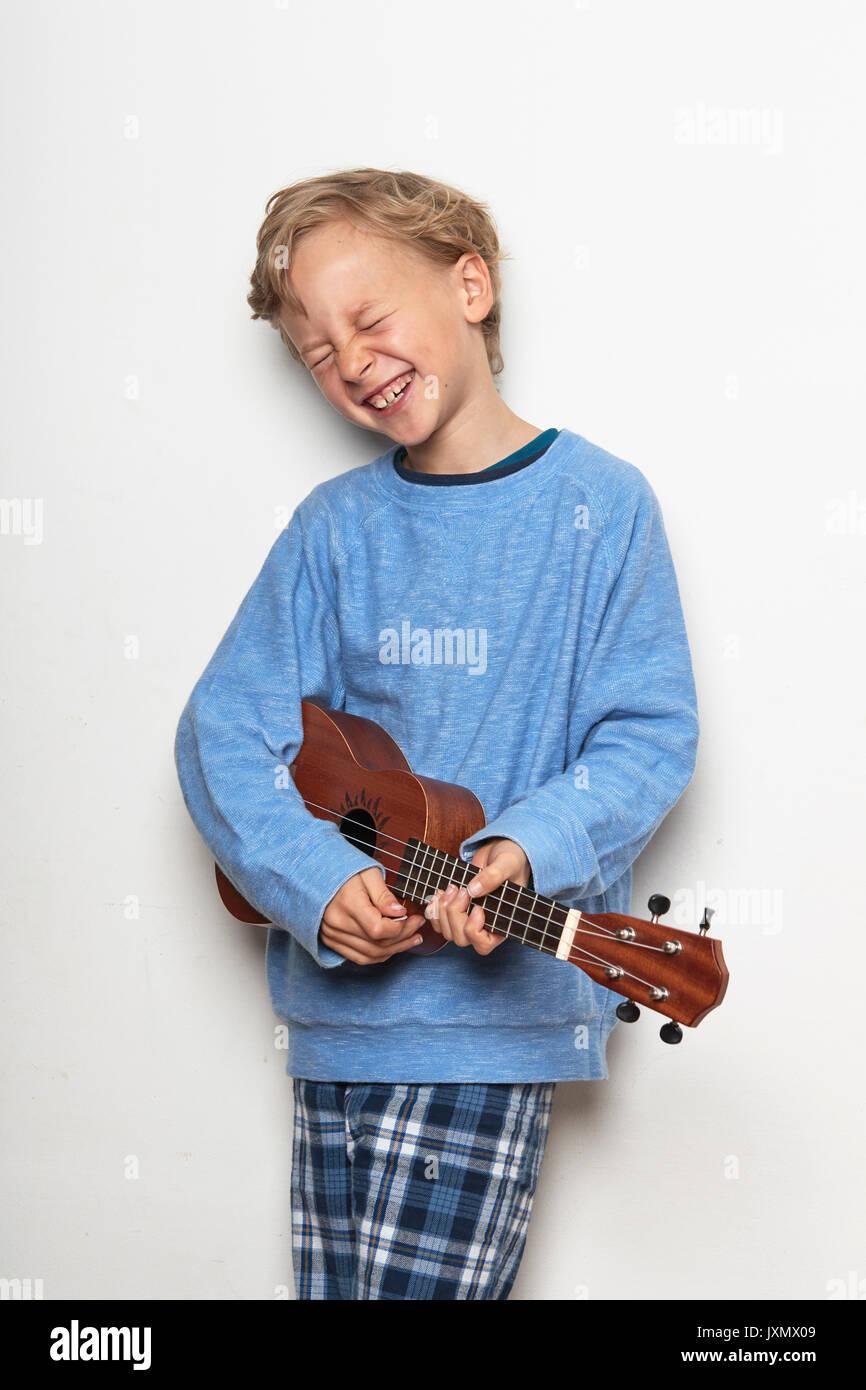 Boy playing ukulele, eyes closed, laughing Stock Photo
