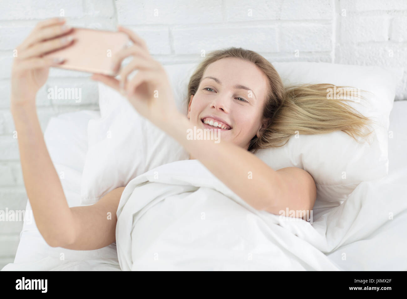 Young woman lying in bed, taking selfie, using smartphone Stock Photo