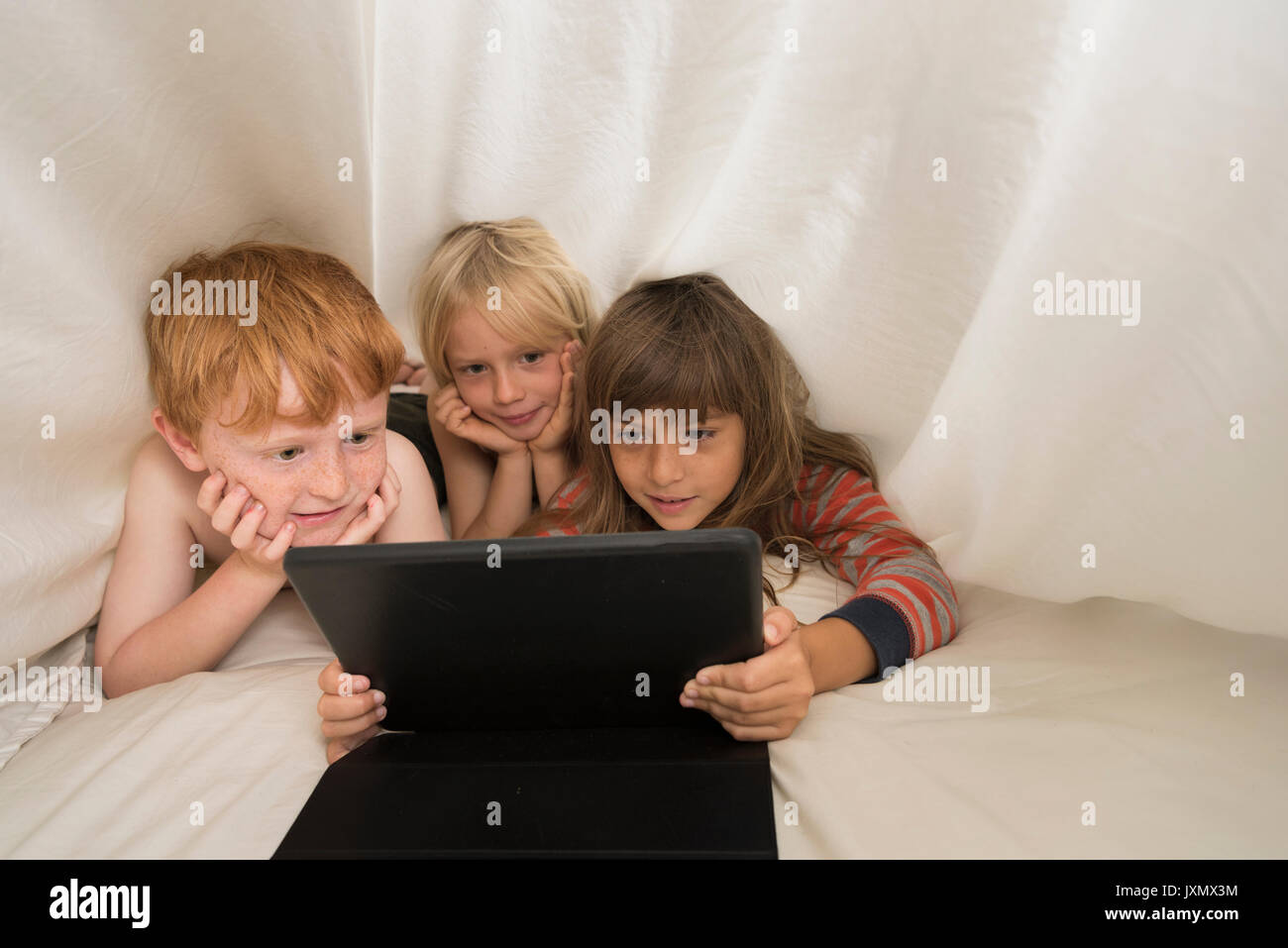 Children lying in bed looking at digital tablet Stock Photo