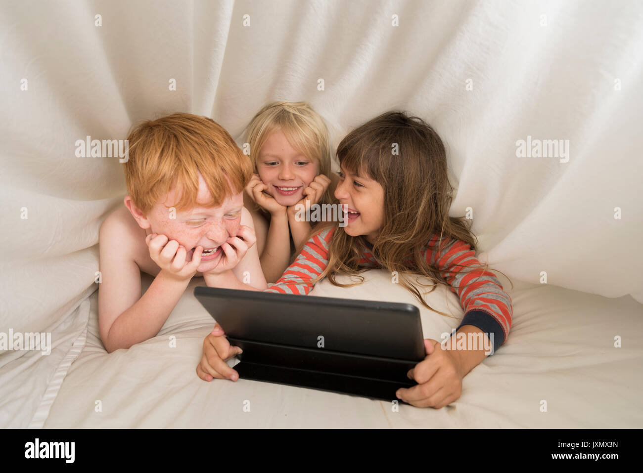 Children lying in bed looking at digital tablet Stock Photo