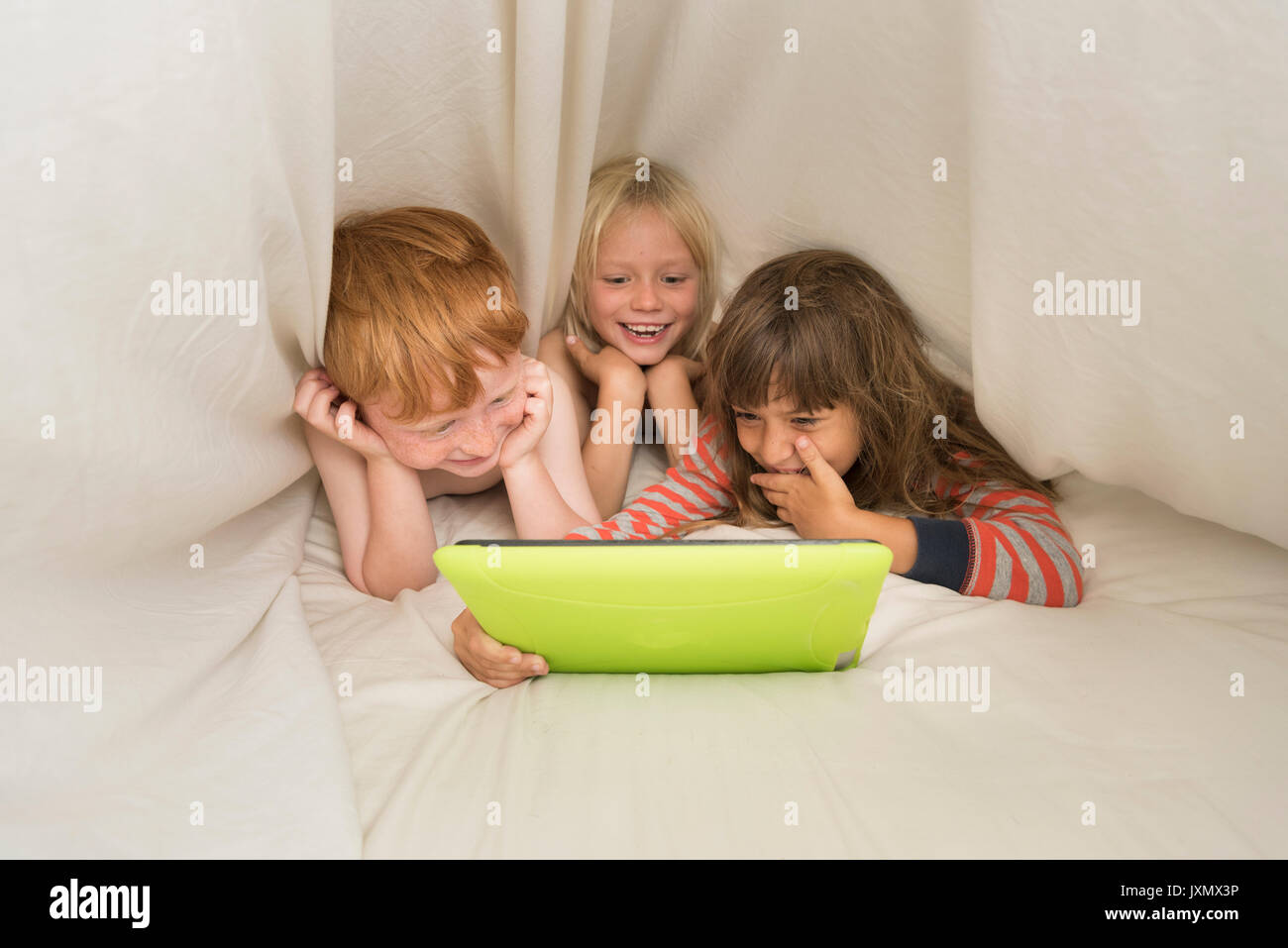 Children lying in bed looking at digital tablet Stock Photo