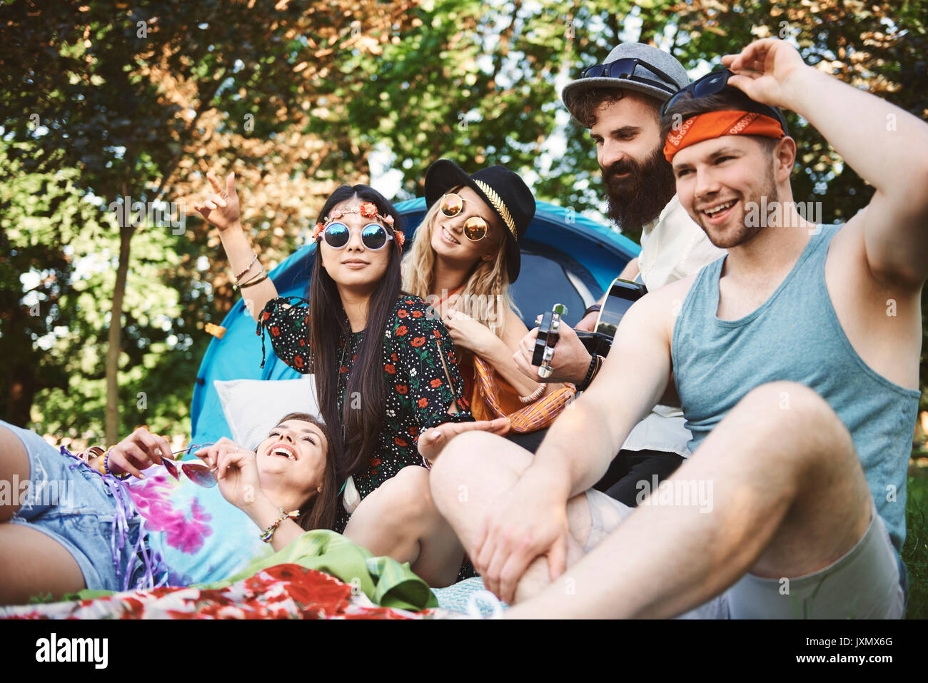 Five young adult friends playing acoustic guitar while festival camping Stock Photo