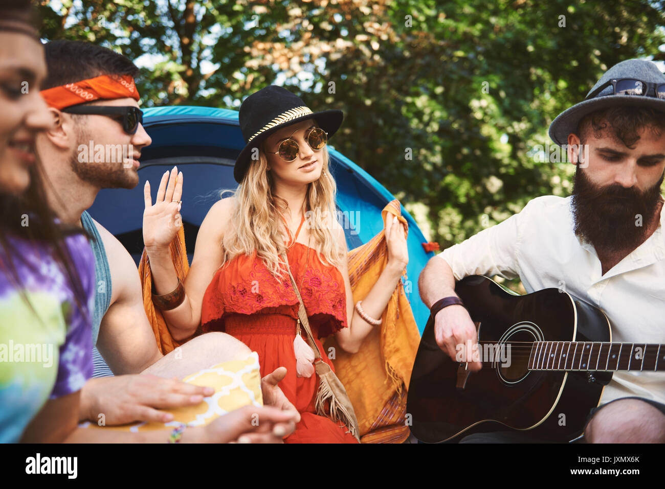 Young adult friends playing acoustic guitar while festival camping Stock Photo