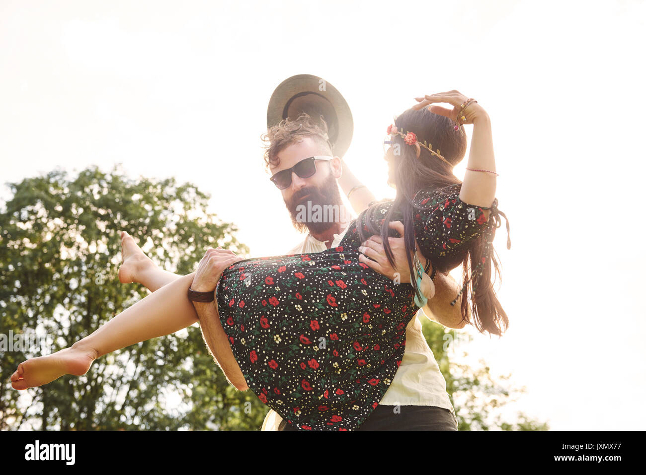 Young man carrying boho girlfriend in arms at festival Stock Photo