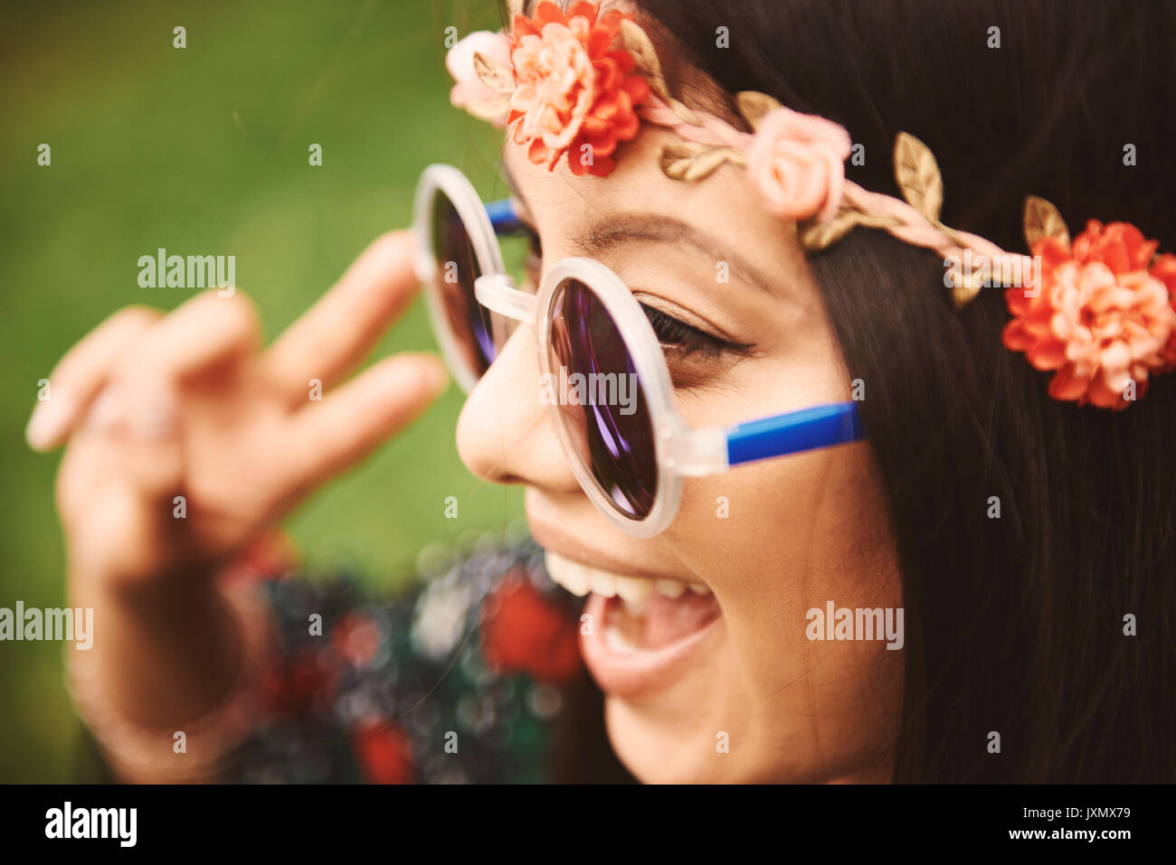 Young hippy woman in floral headband making peace sign at festival Stock Photo