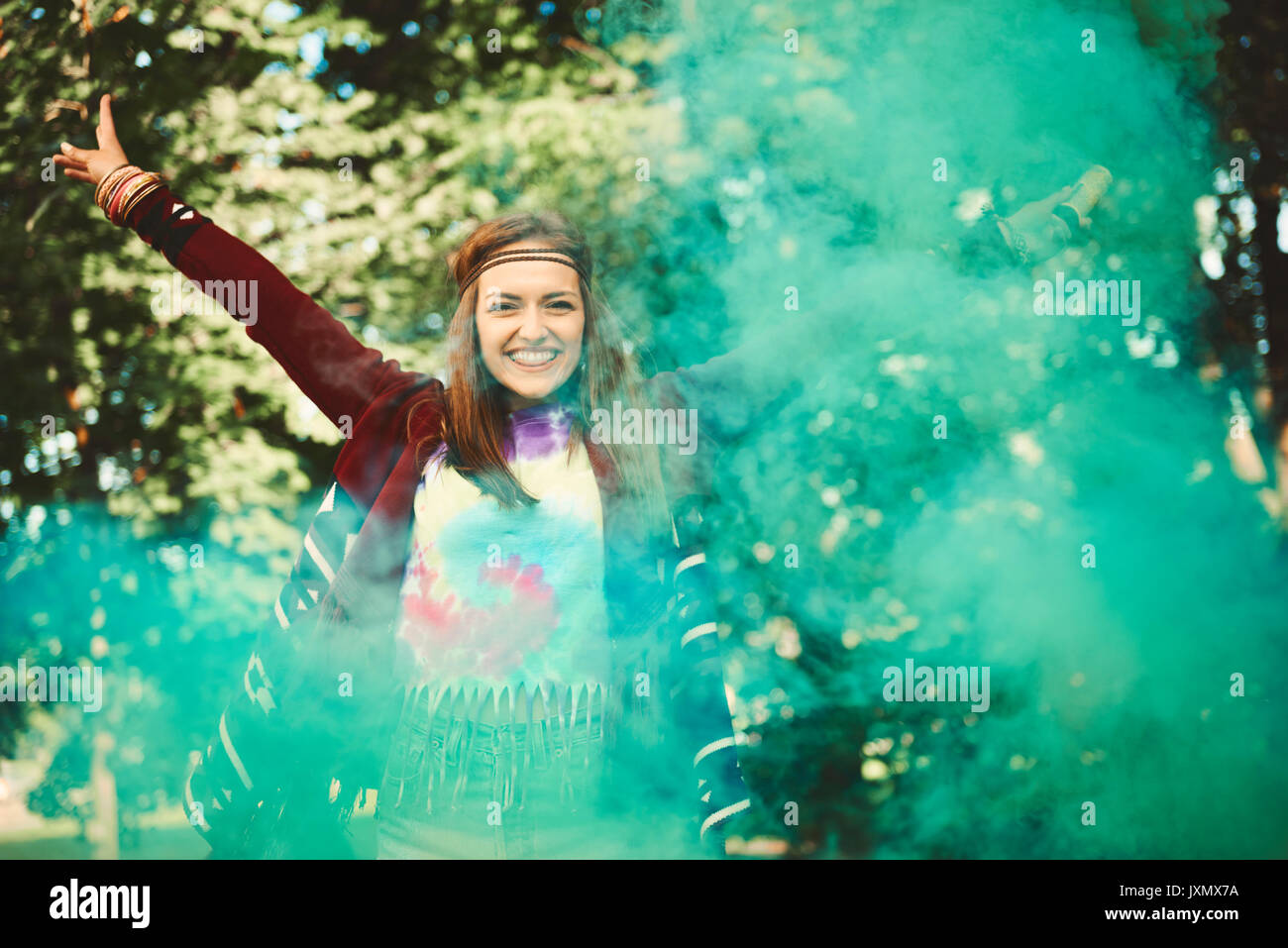 Young boho woman dancing with green smoke flare  at festival Stock Photo