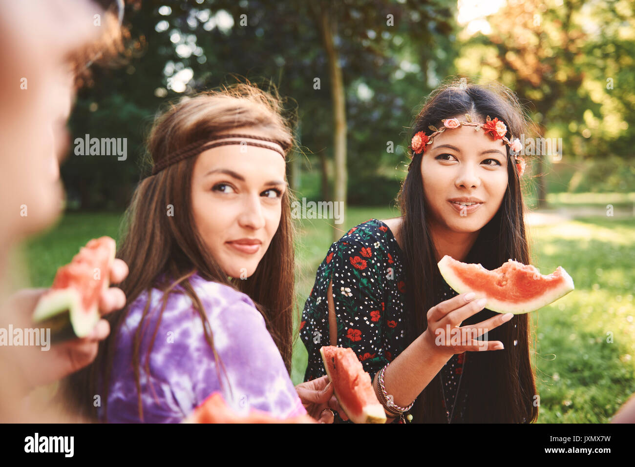 Young boho women eating melon slice at festival Stock Photo