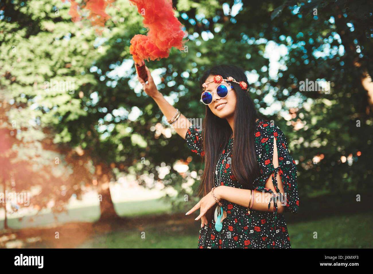 Young boho woman holding up red smoke flare at festival Stock Photo