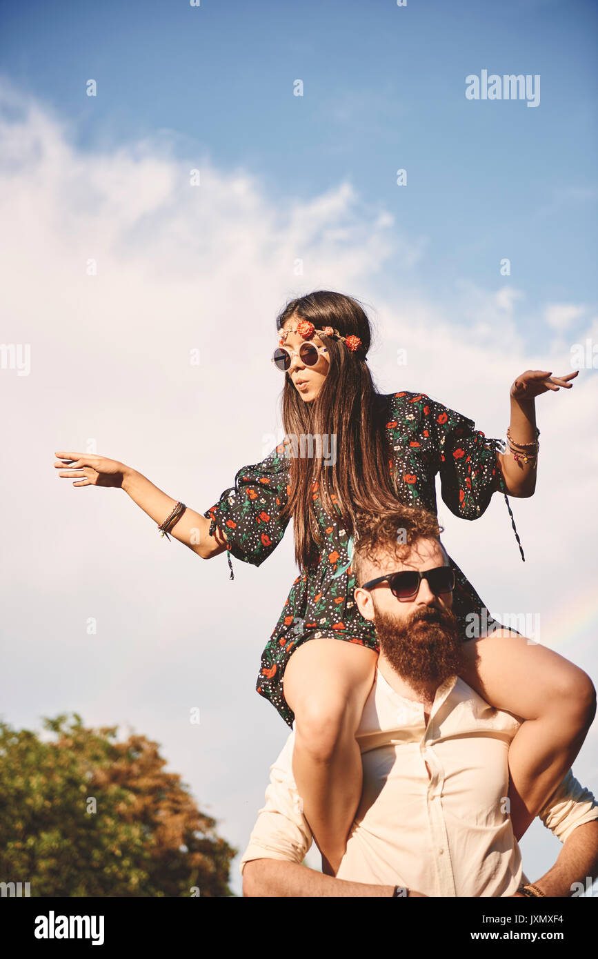 Young boho woman dancing on boyfriend's shoulders at festival Stock Photo