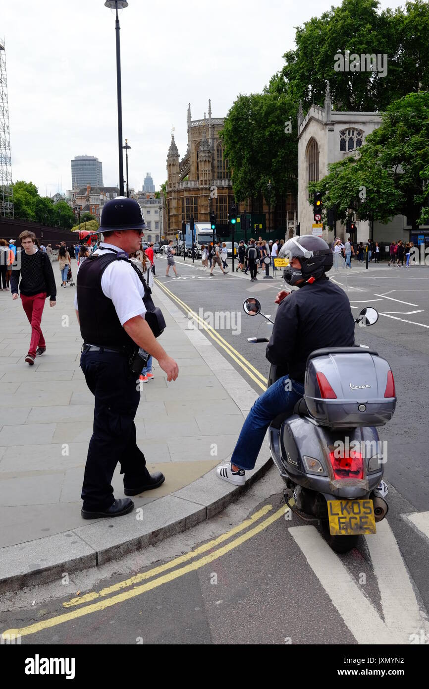 A police officer on duty at the gates to the Houses of Parliamrnt in London, gets a parked moped rider to move on Stock Photo