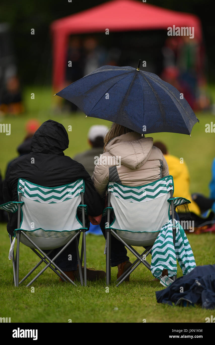 A couple watch local sport in the rain sitting in chairs with umbrella up Stock Photo