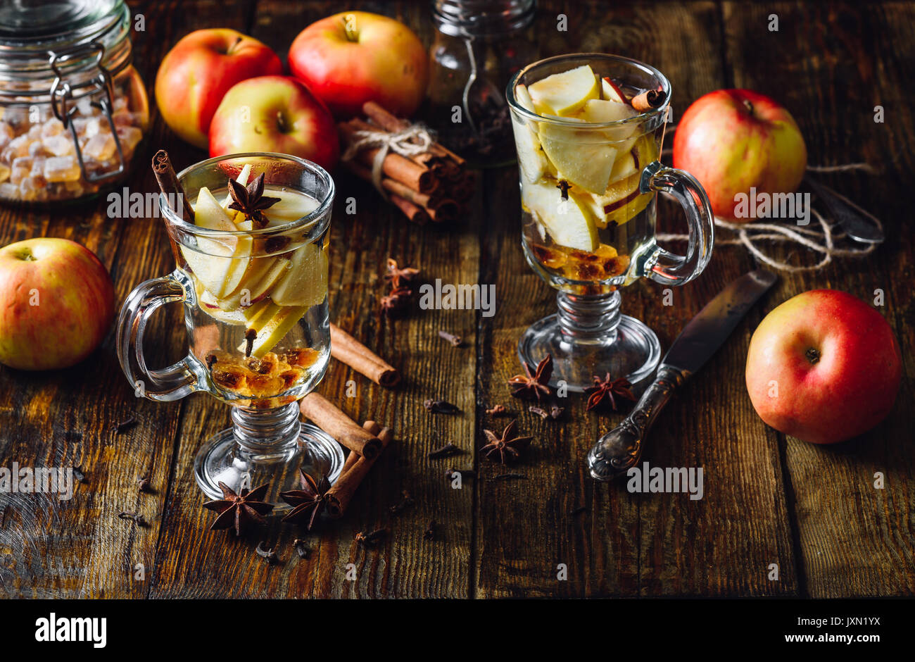 Glasses of Christmas Apple Drink with Clove, Cinnamon, Anise Star and Dark Candy Sugar. All Ingredients and Some Kitchen utensils on Wooden Table. Ver Stock Photo