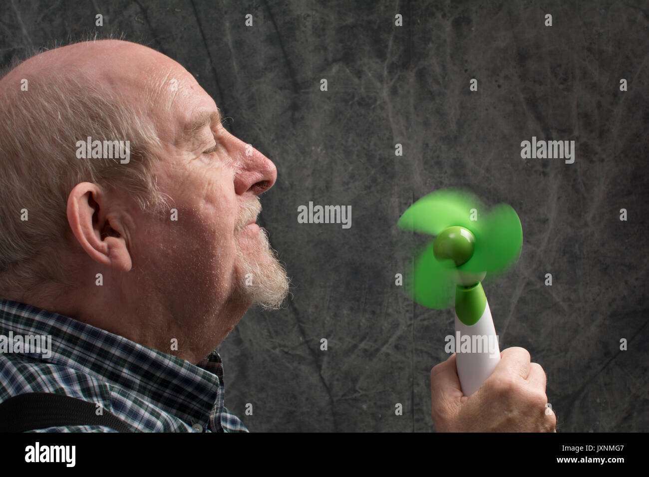 An older man cooling down with a hand held portable fan Stock Photo