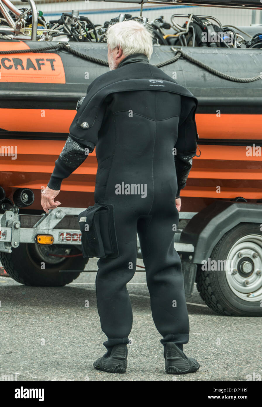 Rear view of an elderly man in a diving suit, next to a rigid inflatable boat (RIB) on a trailer, in Penzance harbour, Cornwall, England, UK. Stock Photo
