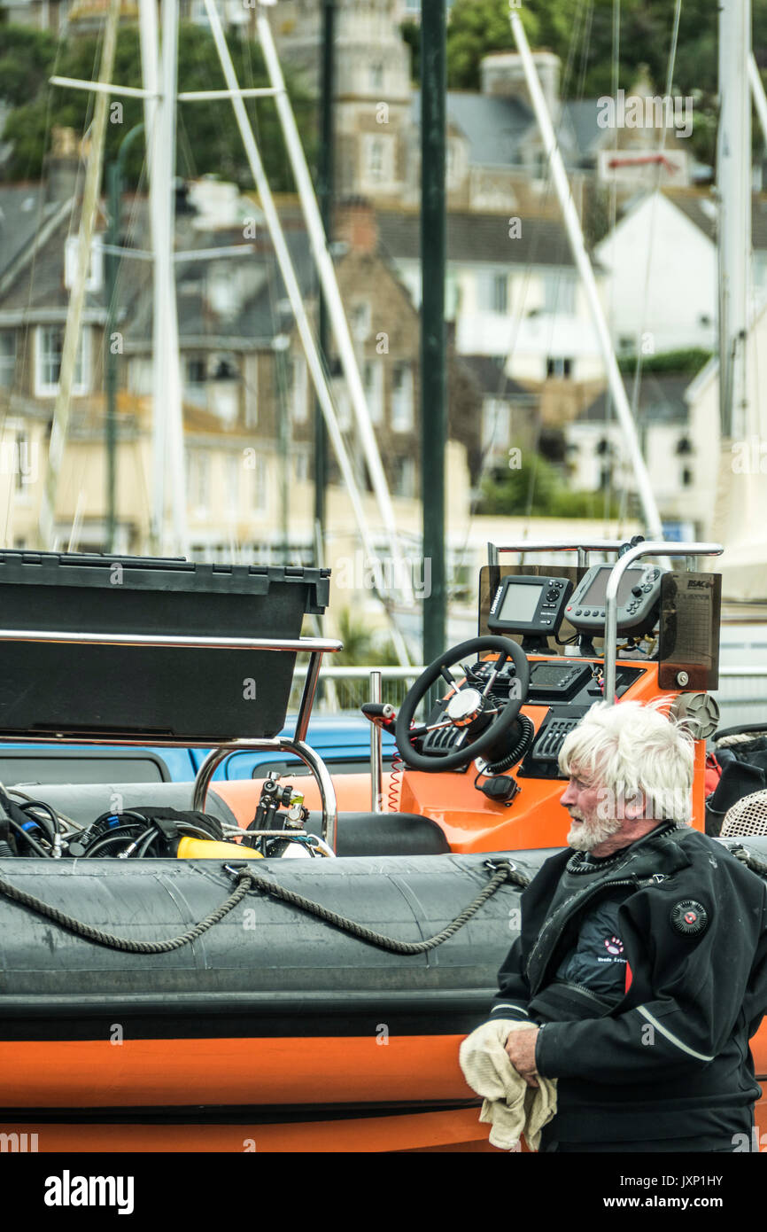 An elderly man in a diving suit, next to a rigid inflatable boat (RIB) on a trailer, in Penzance harbour, Cornwall, England, UK. Stock Photo