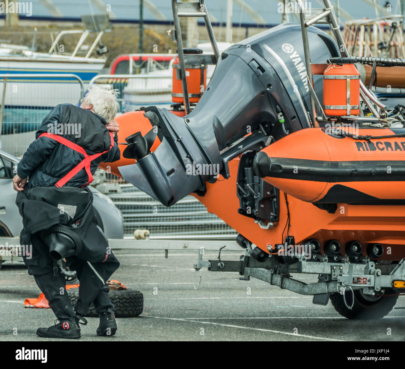 An elderly man squeezing into a diving suit, next to a rigid inflatable boat (RIB) with outboard motor, on a trailer, in Penzance harbour, Stock Photo