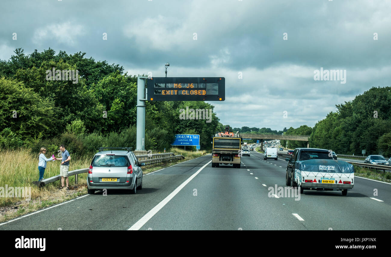 A broken down car and a couple nearby on the hard shoulder of the M6 motorway in the East Midlands, heading west, England, UK. Stock Photo