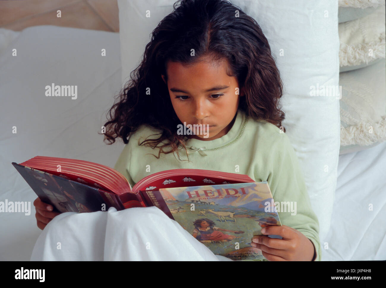 Young little Girl  7-10 year old reading storybook in bed African American/Caucasian Stock Photo