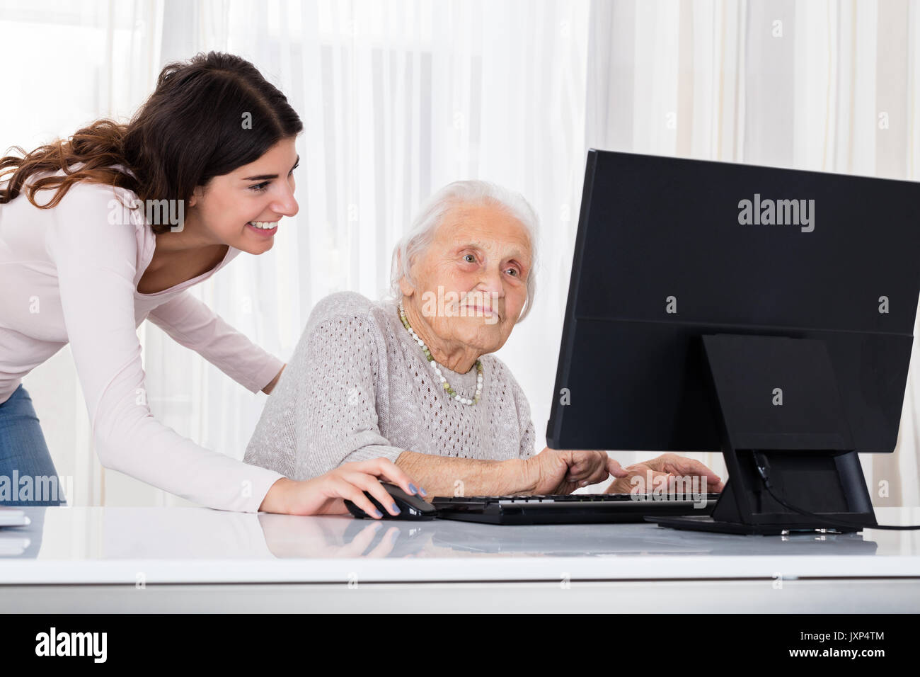 Young Woman Helping Her Grandmother For Using A Laptop On Desk At Home Stock Photo