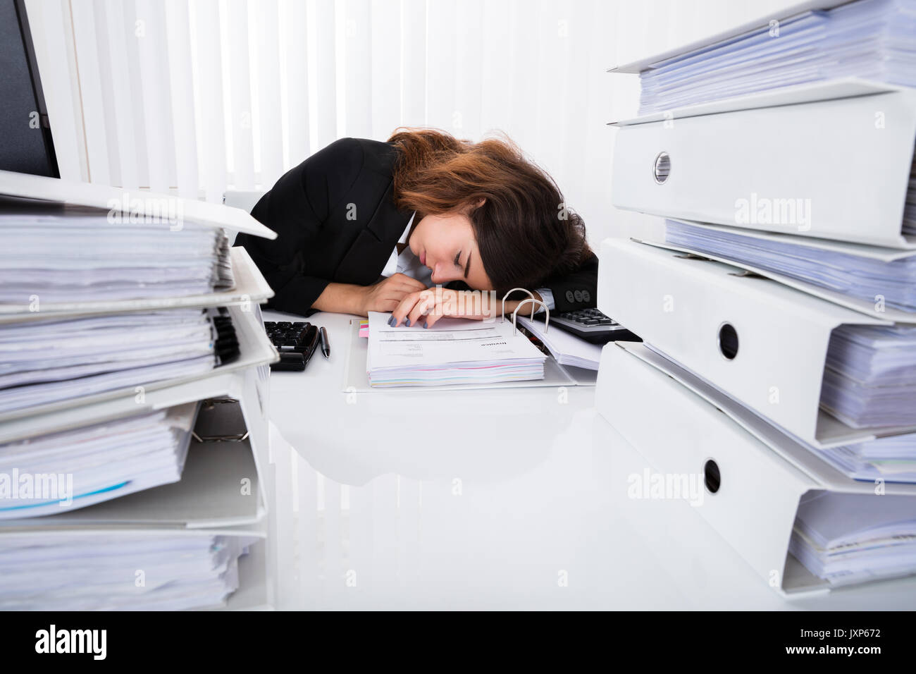 Young Exhausted Businesswoman Sleeping On Desk In Office Stock Photo