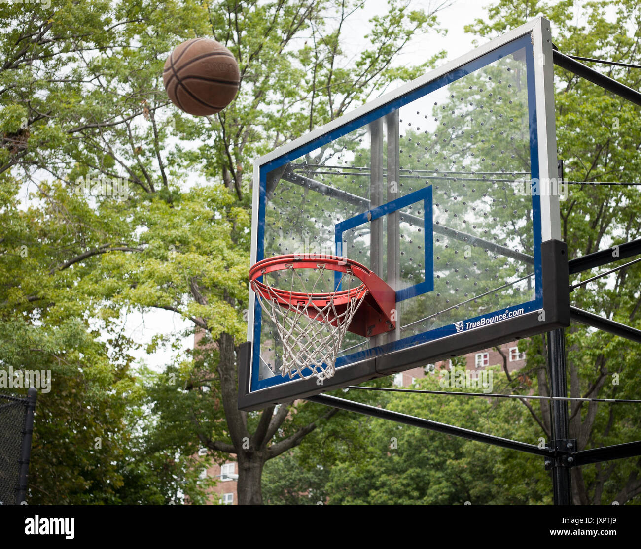 An NBA regulation basketball arcs towards the hoop in a pickup game on a playground. Stock Photo