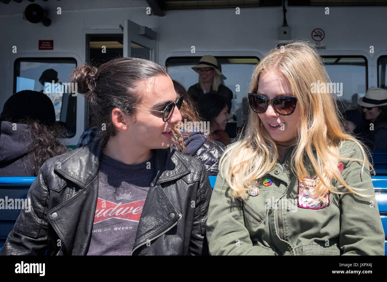 OAKLAND, CA- May 13, 2017: Two hipster millennials talking on the ferry from San Francisco to Oakland. Leather jacket, man bun, sunglasses, political Stock Photo