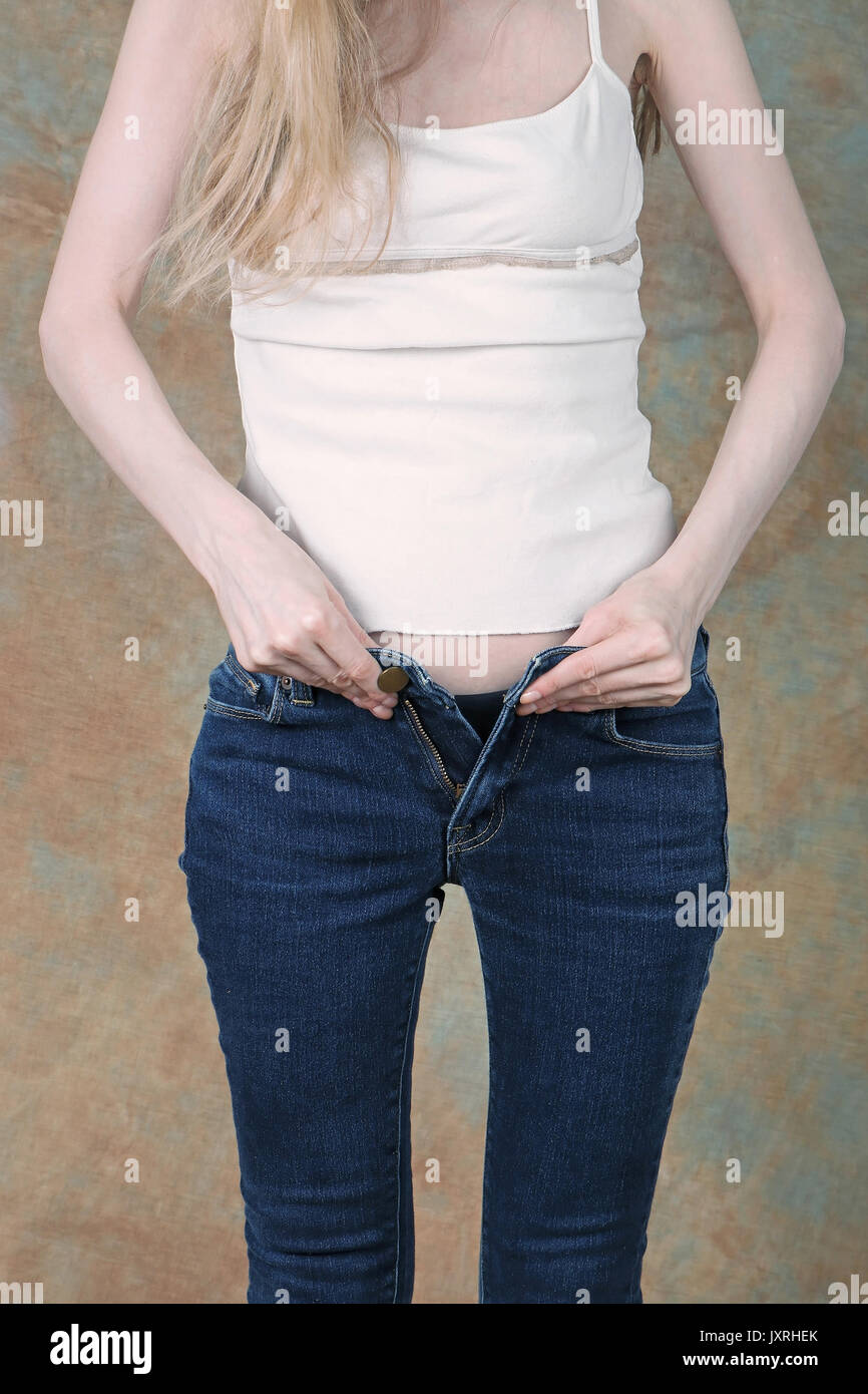 Young girl trying to zip up tight blue jeans Stock Photo