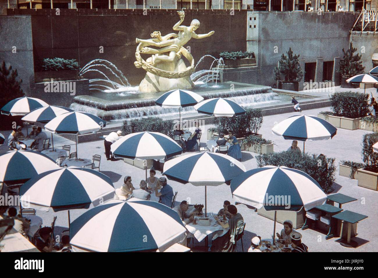 People eating and drinking in The Lower Plaza of the Rockefeller Centre, New York, in 1956. Image shows fashion of the 1950s period. Statue of Prometheus in the background. Stock Photo