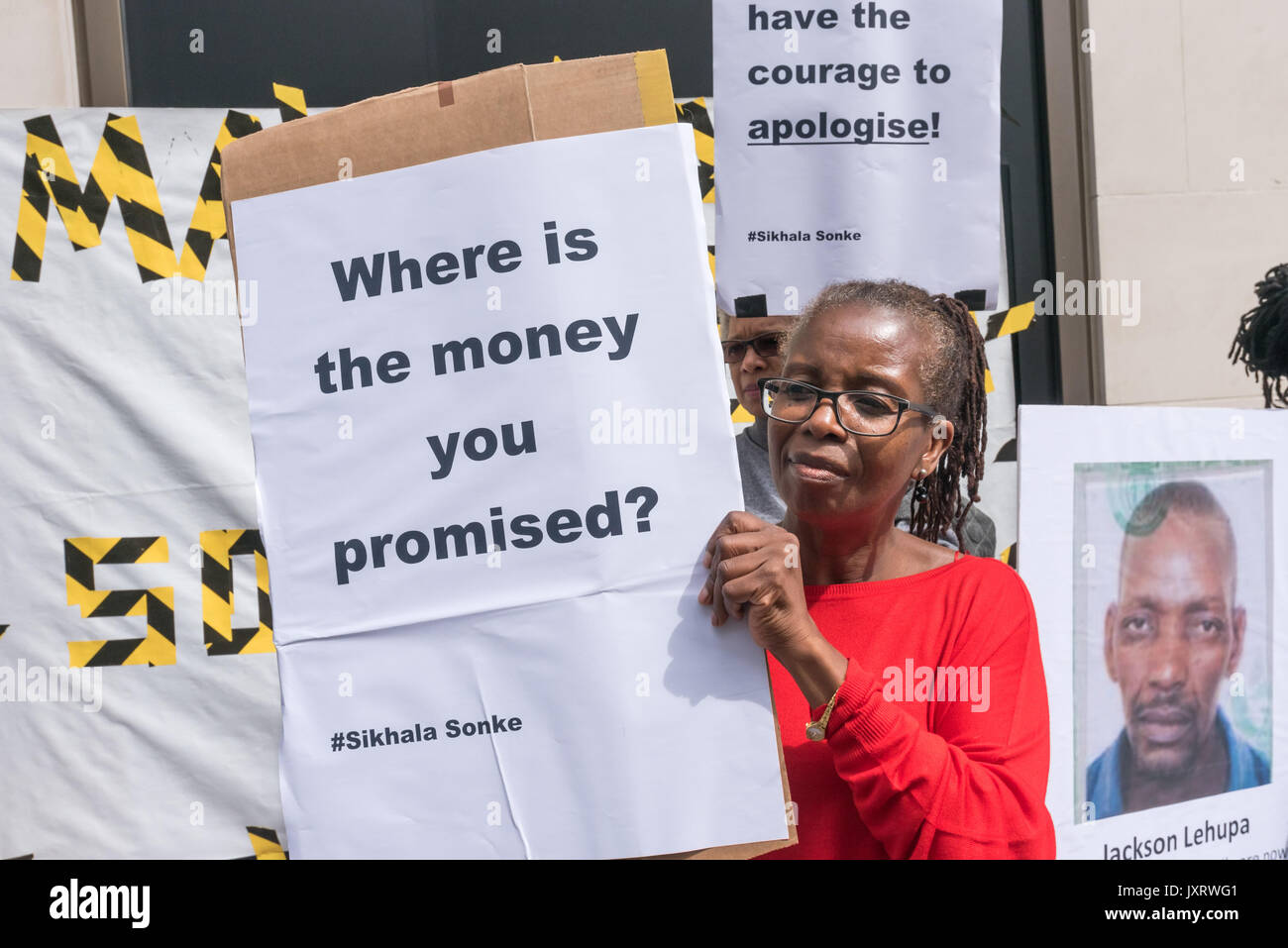 London, UK. 16 August 2017. A woman holds a poster 'Where is the money you promised' ouside Lonmin's London HQ on the 5th anniversary of the massacre when 34 striking miners were shot dead by South African police at Lonmin's Marikana platinum mine. Although some state compensation has been offered, none has yet been paid. Credit: Peter Marshall/Alamy Live News Stock Photo