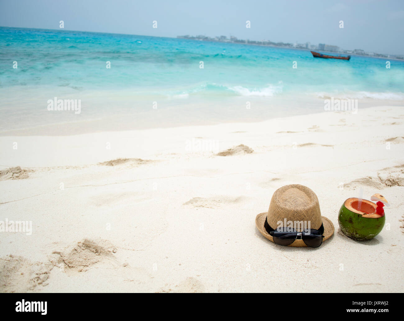 Summer hat and sunglasses with coconut on a sunny beach. Stock Photo