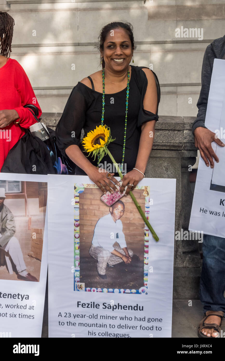 London, UK. 16th August 2017. A woman holds a sunflower and a poster of one of the miners who was killed at the protest vigil outside the South African High Commission in Trafalgar Square on the 5th anniversary of the massacre when 34 striking miners were shot dead by South African police at Lonmin's Marikana platinum mine. Credit: Peter Marshall/Alamy Live News Stock Photo