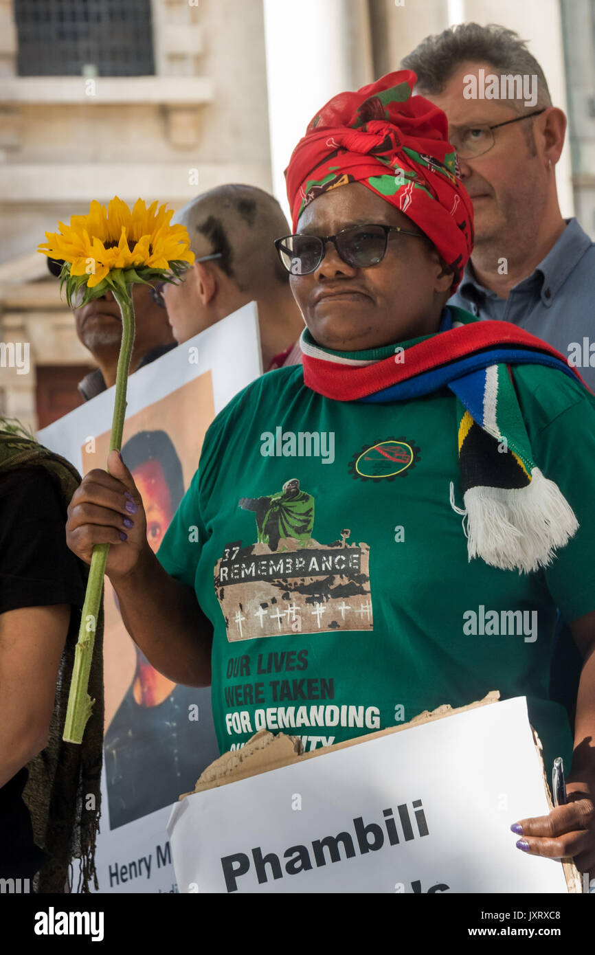 London, UK. 16th August 2017. Primrose Nokulunga Sonti holds a sunflower and poster at the protest vigil outside the South African High Commission in Trafalgar Square on the 5th anniversary of the massacre when 34 striking miners were shot dead by South African police at Lonmin's Marikana platinum mine. Credit: Peter Marshall/Alamy Live News Stock Photo