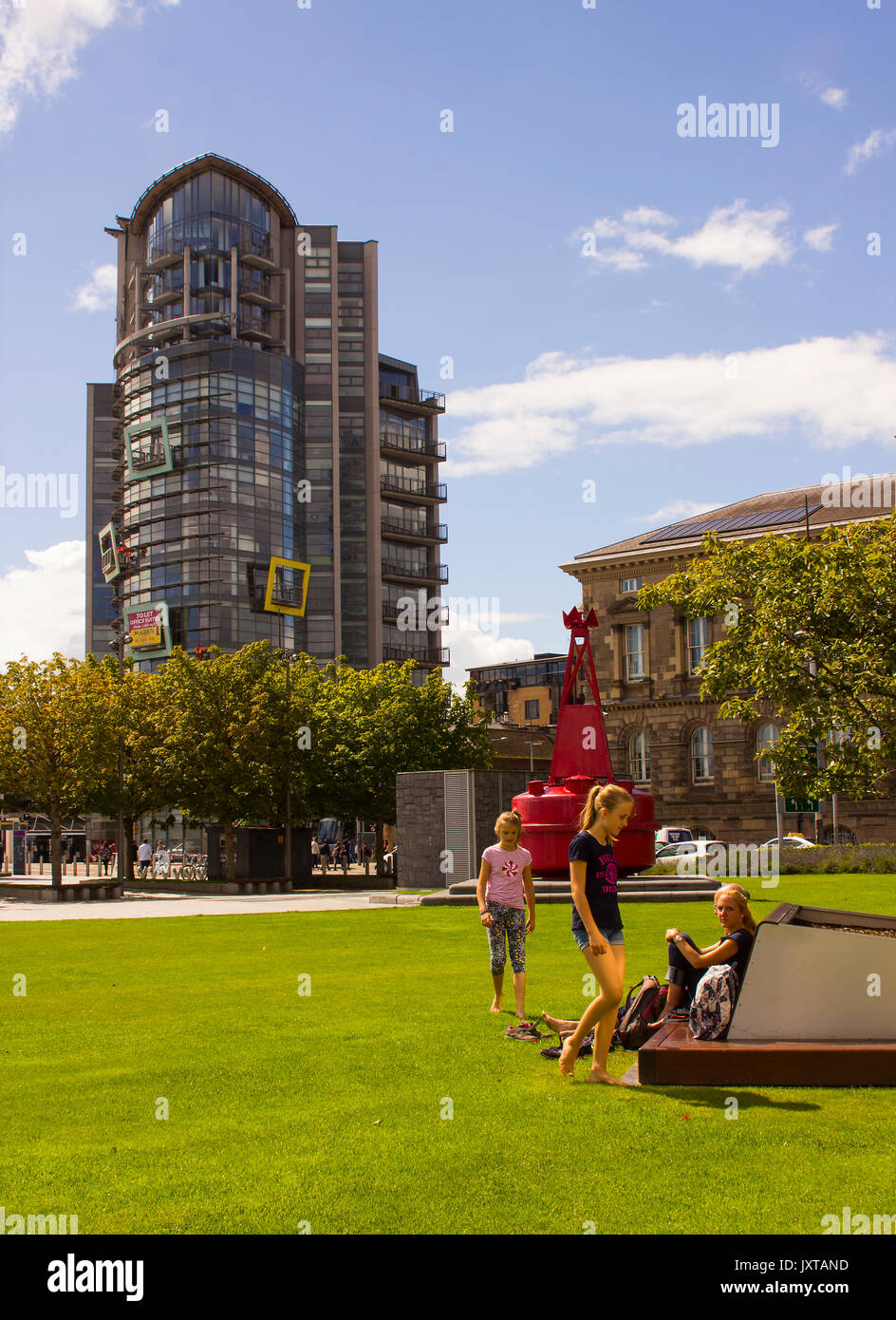 A modern high rise office block and the historic Customs House building close to Donegall Quay with a mother and children relaxing and playing Stock Photo
