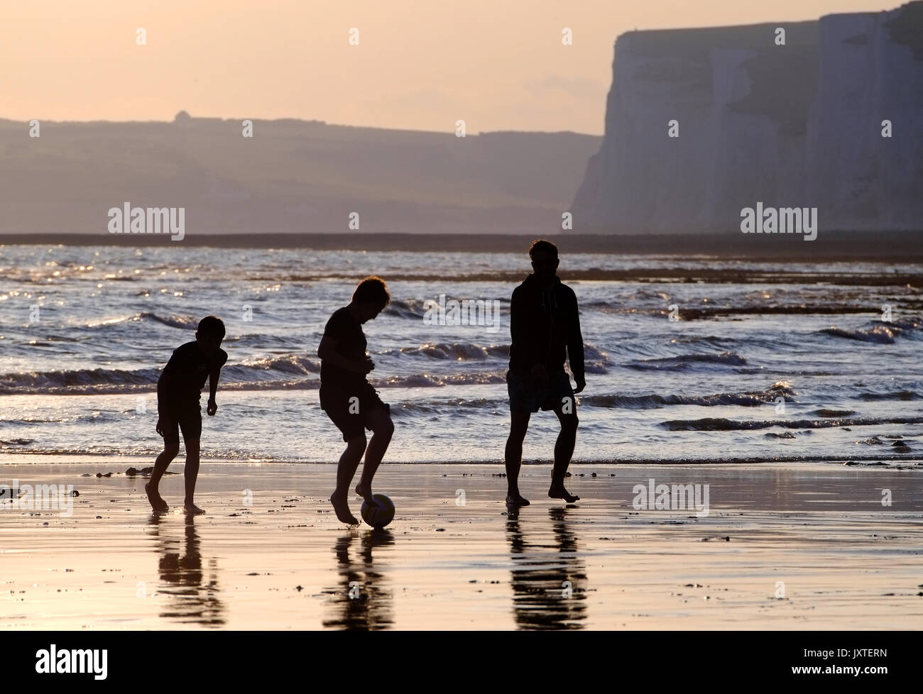 Father and sons playing ball games on a beach at sunset, Seven Sisters, South Downs National Park, East Sussex Stock Photo